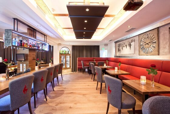 Innenansicht der Reisch Bar Innenansicht einer Bar mit Holztischen, grauen Polsterstühlen und einer langen roten Sitzbank.