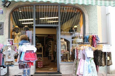 Eingangsbereich eines Modegeschäfts mit Trachtenmode auf Kleiderständern im Außenbereich.