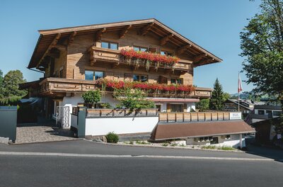 Mehrstöckiges Holzhaus mit Blumenbalkonen an einer asphaltierten Straße unter blauem Himmel.