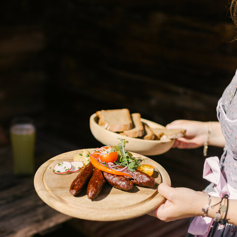 In Kitzbühel trägt eine Bedienung in traditionellem Gasthaus zwei Holzbretter mit Würstchen, Gemüse und Brot.