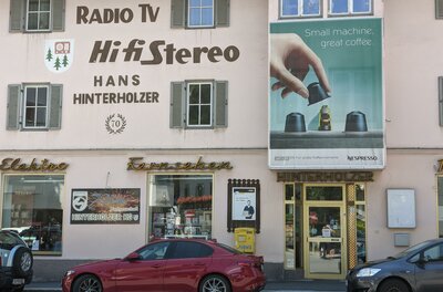Ein Geschäft mit einem großen Schild für HiFi-Geräte und Elektrotechnik. Nebenan ist eine Werbung für Nespresso-Kaffeemaschinen.