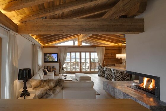 Wohnzimmer Chalet Bockberg Moderner Wohnraum in einer Holzhütte mit Kamin, weißem Sofa und sichtbaren Dachbalken.