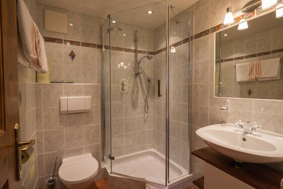 Badezimmer Ferienwohnung Hauser Badezimmer mit Glasdusche, Waschbecken, Spiegel und Toilette in einer Ferienwohnung.