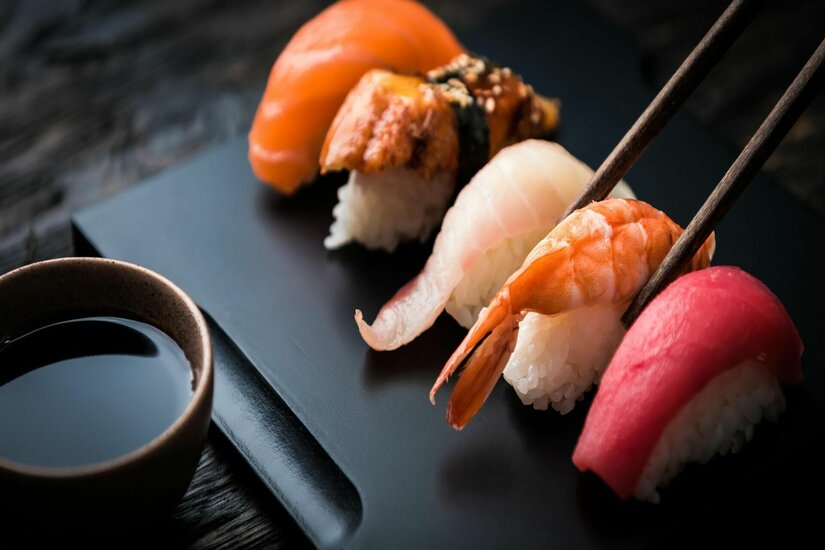 Verschiedene Nigiri-Sushi auf einer schwarzen Platte mit Stäbchen und Sojasauce.