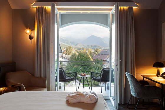 Blick aus einem Hotelzimmer durch eine offene Balkontür auf Berge und Bäume.