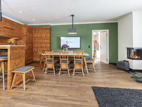 Essbereich im Kitzbühel Country Club Moderner Essbereich mit Holztisch, grüner Wand, TV und Kamin in einer Ferienwohnung.
