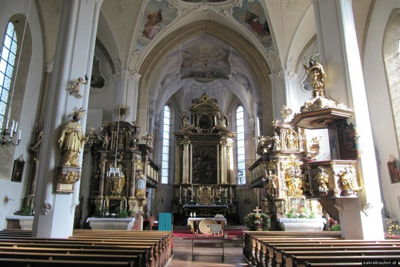 Innenansicht einer barocken Kirche mit goldenem Hochaltar, Kanzel, Kirchenbänken und Deckenmalereien.