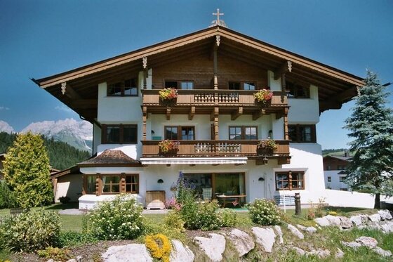 Sommer aussen Ponapart Dreistöckiges alpines Gästehaus mit Holzbalkonen, Blumenschmuck und Garten vor Bergkulisse.