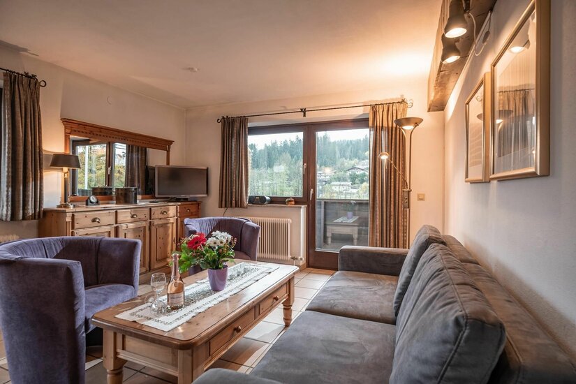 Wohnbereich Appartement Hornblick Wohnzimmer mit grauer Couch, Holztisch, zwei Sesseln und Balkontür mit Blick auf bewaldete Berge.