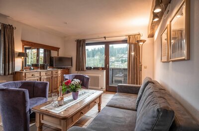 Wohnbereich Appartement Hornblick Wohnzimmer mit grauer Couch, Holztisch, zwei Sesseln und Balkontür mit Blick auf bewaldete Berge.