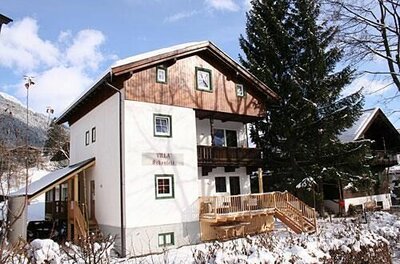 Zweistöckiges weißes Gebäude mit Holzgiebel und Balkon in einer verschneiten Winterlandschaft.