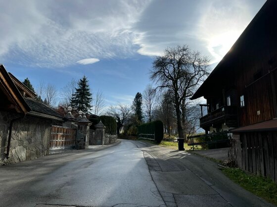 Asphaltierte Straße zwischen traditionellen Holzhäusern und Steinmauern unter bewölktem Himmel.