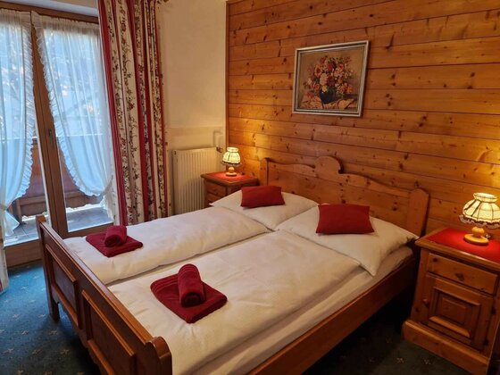 Schlafzimmer Pension Alpenrose Doppelbett aus Holz in einem Zimmer mit holzgetäfelten Wänden und Balkonzugang.