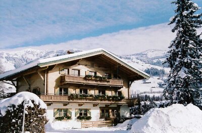 Alpines Holzhaus mit Balkonen im Schnee vor bewaldeten Bergen.