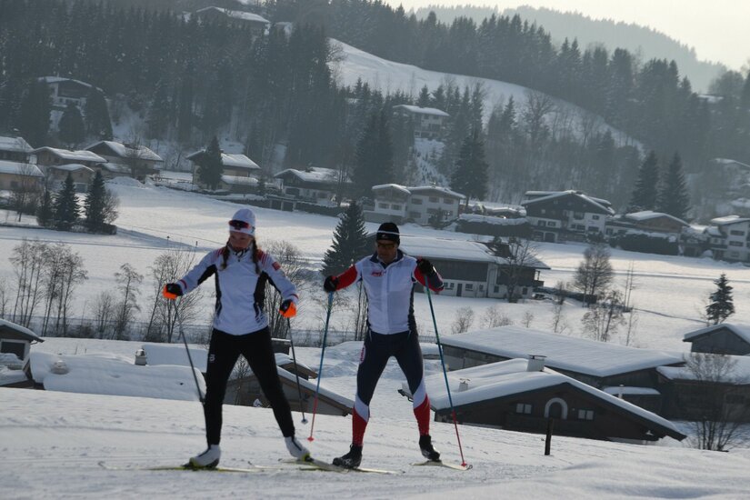 Langläufer auf der Sportloipe Zwei Personen beim Skilanglauf auf einer verschneiten Loipe vor einer dörflichen Kulisse.