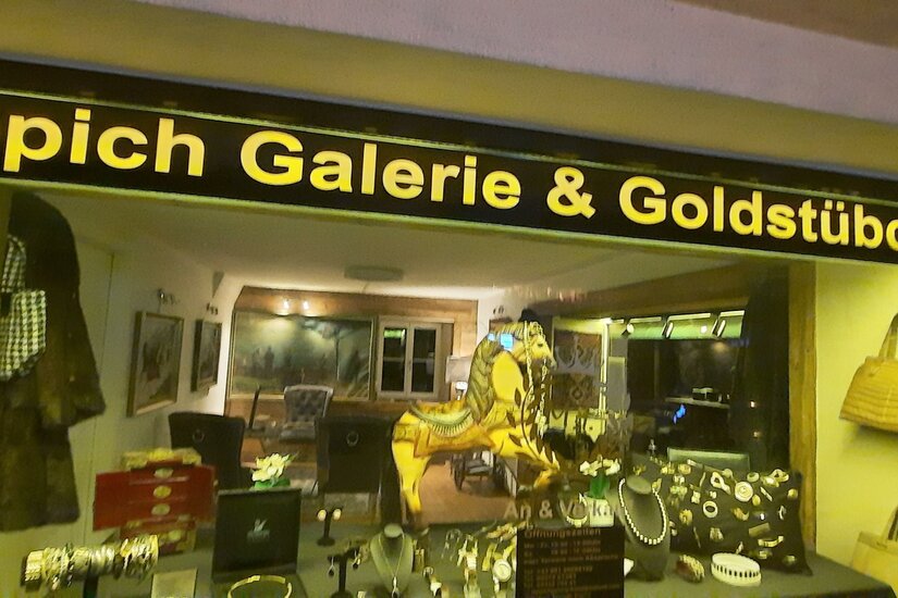 Ein Schaufenster mit der Aufschrift „Teppich Galerie & Goldstückchen“. Die Ausstellung zeigt Schmuck und Accessoires.