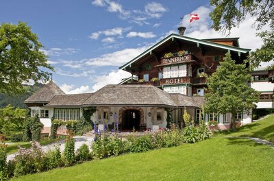 Außenansicht des Hotel Tennerhof mit Holzfassade, Blumenbeeten und österreichischer Flagge unter blauem Himmel.
