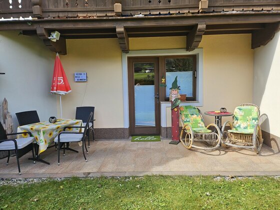 Tamara's Apart Terrasse Gepflasterte Terrasse mit Esstisch, Stühlen und zwei Schaukelstühlen vor einer Hauswand.