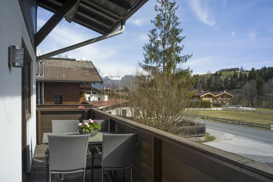 Balkon Appartement Hornblick Holzbalkon mit Sitzgruppe, Blick auf eine Straße, Häuser und schneebedeckte Berge im Hintergrund.