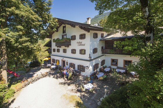 Gasthof Jodlbühel im Sommer Außenansicht des Gasthof Jodlbühel mit bewirtschafteter Terrasse, Fahrrädern und Spielplatz unter Bäumen.