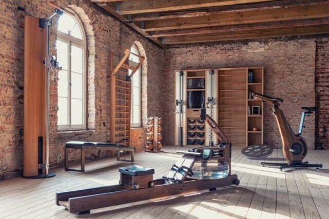 Bodyfit Fitnessraum Fitnessraum mit Holzgeräten, Rudermaschine und Ergometer vor einer Ziegelwand.