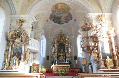 Ein prächtiges Kircheninnere mit einer beeindruckenden Altaranlage und kunstvollen Verzierungen. Die bunten Fresken und das goldene Dekor verleihen dem Raum eine festliche Atmosphäre.