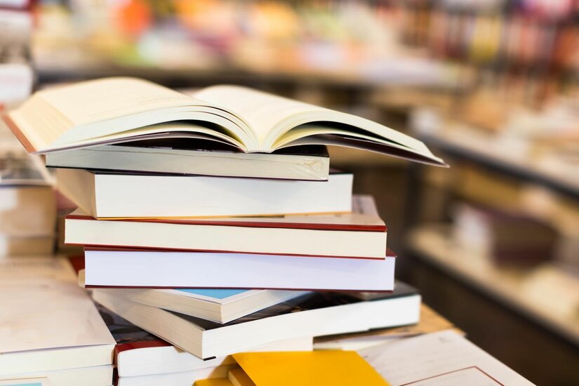 Bücherei Kolpinghaus Ein Stapel verschiedener Bücher mit einem aufgeschlagenen Buch obenauf in einer Bücherei.