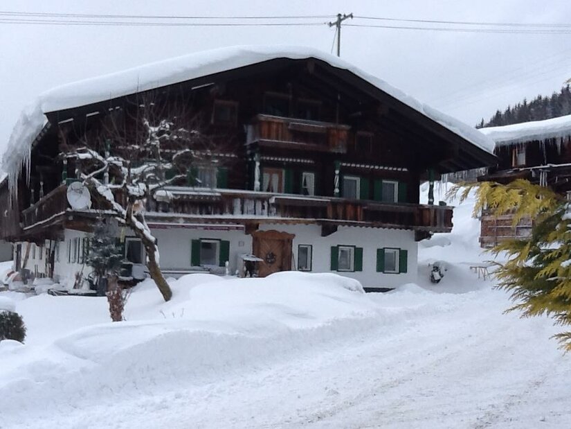 Traditionelles Alpenhaus aus Holz und Stein mit schneebedecktem Dach im Winter.