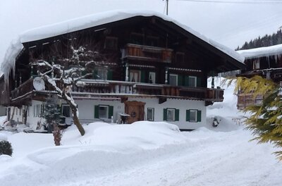 Traditionelles Alpenhaus aus Holz und Stein mit schneebedecktem Dach im Winter.