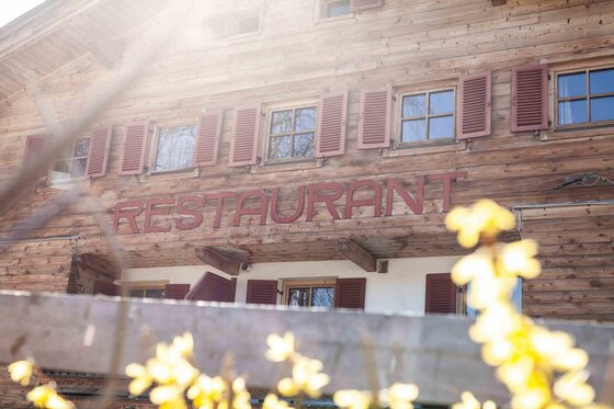 Holzfassade eines alpinen Gebäudes mit dem Schriftzug Restaurant und roten Fensterläden.