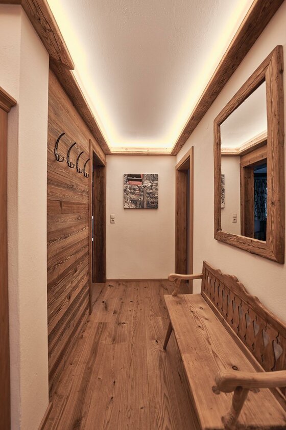 Flur der Ferienwohnung Hahnenkammblick Flur mit Holzboden, Holzbank, Garderobenhaken und indirekter Deckenbeleuchtung.