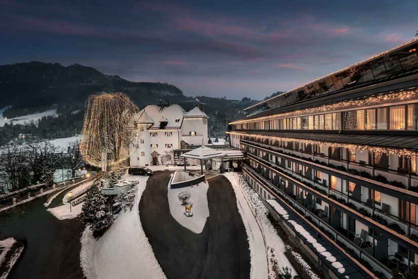 Ein charmantes Hotel in einer malerischen Winterlandschaft, umgeben von schneebedeckten Bergen. Die warme Beleuchtung der Fenster schafft eine einladende Atmosphäre.