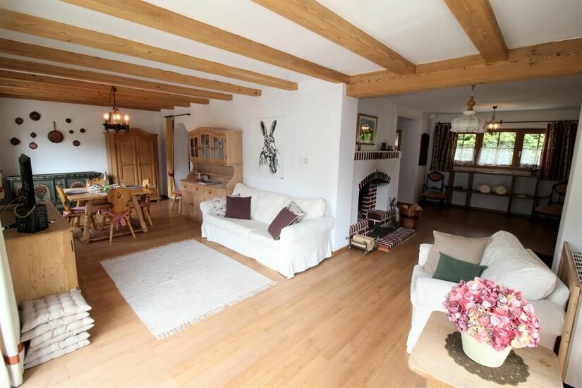 Wohnbereich Lodge 11 Wohnzimmer mit weißen Sofas, Holzbalkendecke, Kamin und Essbereich im Hintergrund.