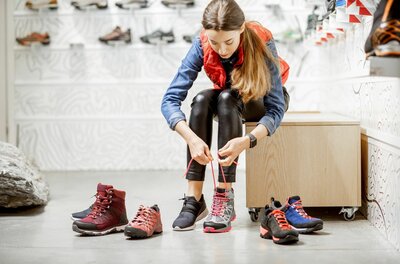 Eine Frau sitzt in einem Sportgeschäft und schnürt einen grauen Wanderschuh.