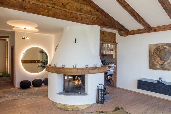 Moderner Kamin in einem Wohnraum mit Holzbalkendecke und indirekt beleuchtetem Spiegel.