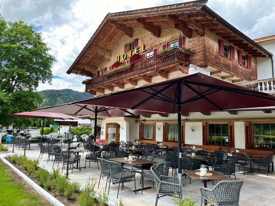 Außenterrasse eines Hotels mit dunklen Sonnenschirmen, Sitzgruppen und Holzfassade im alpinen Stil.