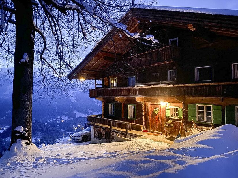 920F1AE6-0891-46B9-8EEE-7CDA3BAFB7F4_1_105_c Ein charmantes Holzhaus im Winter mit einer schneebedeckten Umgebung. Sanftes Licht strahlt aus dem Fenster und schafft eine gemütliche Atmosphäre.