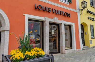 Außenansicht eines Louis Vuitton Geschäfts mit orangefarbener Fassade und gelben Blumen im Vordergrund.