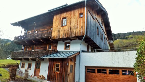 Mehrstöckiges alpines Gebäude mit Holzfassade, Balkonen und einem Garagentor aus Holz.
