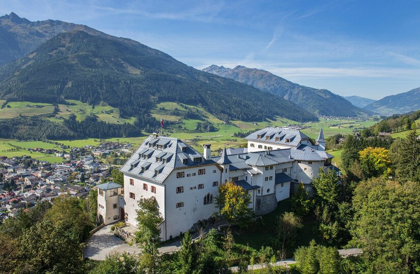 Luftaufnahme von Schloss Mittersill vor bewaldeten Bergen und einer Ortschaft im Tal.