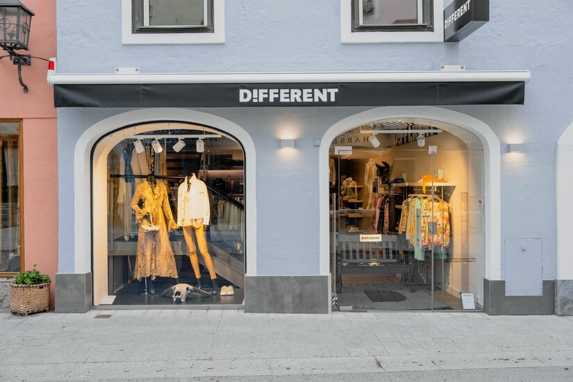 Different Fashion Boutique Außenansicht eines Modegeschäfts mit zwei bogenförmigen Schaufenstern und schwarzer Markise.