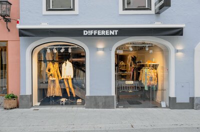Different Fashion Boutique Außenansicht eines Modegeschäfts mit zwei bogenförmigen Schaufenstern und schwarzer Markise.