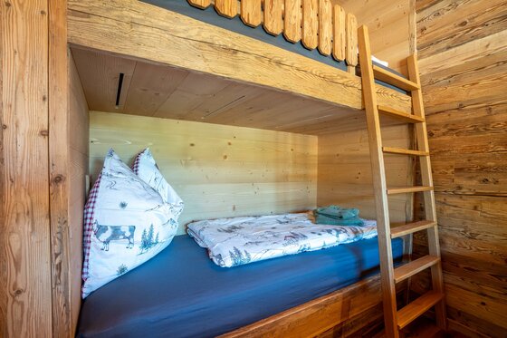 Schlafzimmer im Apartment Taxer Stockbett aus hellem Holz in einer rustikalen Holzhütte mit gemusterter Bettwäsche.