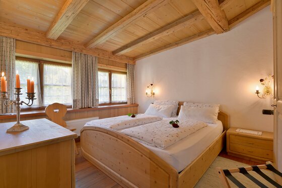 Schlafzimmer im Ploderhaus Rustikales Schlafzimmer mit Doppelbett aus Holz, Holzbalkendecke und zwei Fenstern.