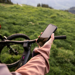 Eine Person steht mit einem Mountainbike am Hahnenkamm in Kitzbühel und schaut auf dem Smartphone in der FAZUA App Informationen zu ihrer E-Bike-Tour an.