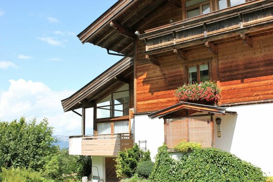 Haus 1 Kitzbühel Apartments Mehrstöckiges alpines Holzhaus mit Balkonen und Blumenkästen vor blauem Himmel.