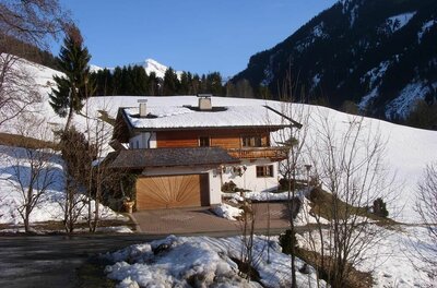 Außenansicht Haus Christina im Winter Alpines Wohnhaus mit Holzfassade und schneebedecktem Dach vor bewaldeten Bergen.