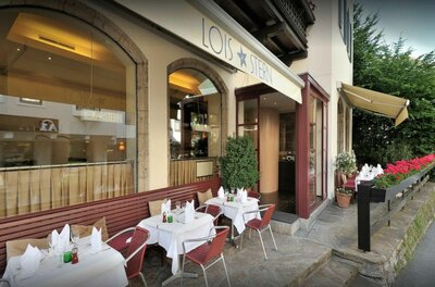 Außenansicht des Restaurants Lois Stern mit gedeckten Tischen auf einer Terrasse unter einer Markise.