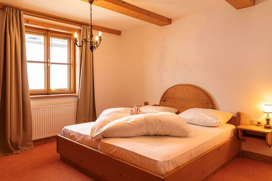 Rustikales Doppelbett aus Holz in einem Zimmer mit Holzbalkendecke und Fenster.