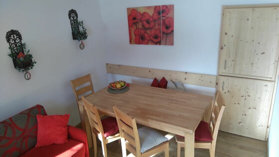 Holztisch mit vier Stühlen, einer Eckbank und einem roten Sofa in einem hellen Raum.